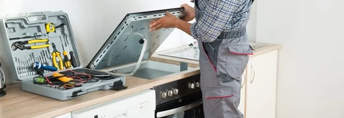 Cooktop repair technician lifting a built-in stovetop for service in Minneapolis, MN