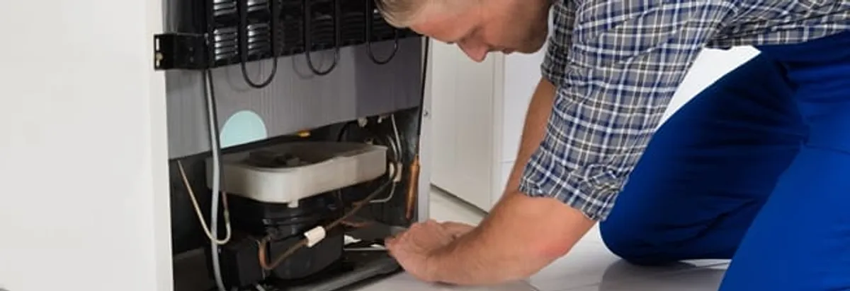 Refrigerator repair technician servicing the compressor and condenser area in Minneapolis, MN