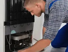 Refrigerator repair technician servicing the compressor and condenser area in Minneapolis, MN
