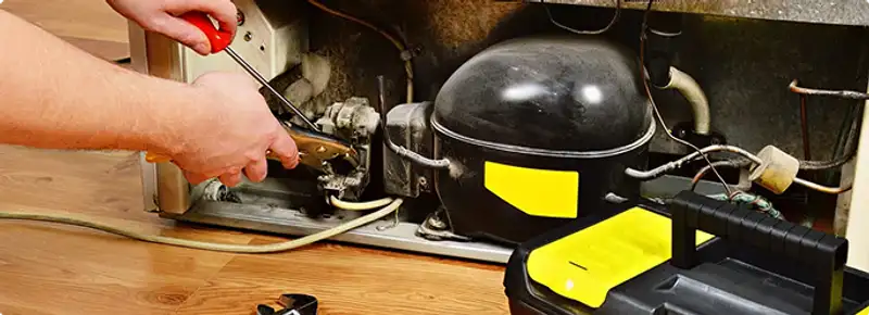 Refrigerator repair technician fixing the compressor and wiring in Minneapolis, MN